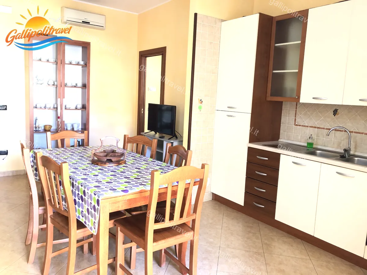 Soggiorno del Trilocale D1/3 con credenza in legno, cucina bianca e TV
