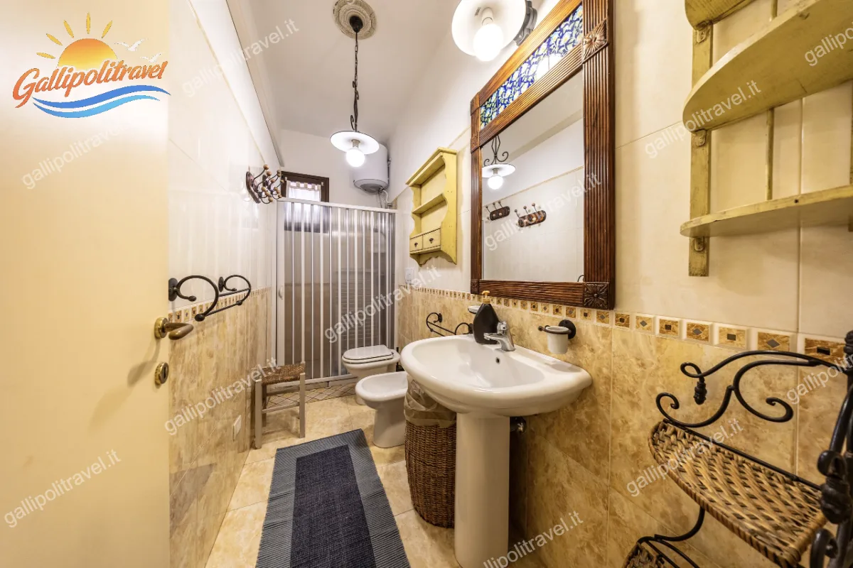 Bagno completo e funzionale con rivestimenti dai toni caldi, dotato di lavabo a colonna, sanitari, box doccia a soffietto e un grazioso specchio con cornice in legno e dettagli colorati