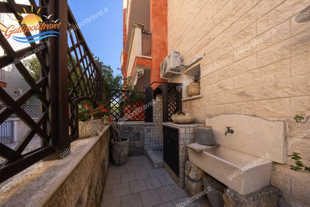 Dettaglio del cortile esterno privato con comodo lavabo in pietra, piante decorative e staccionata in legno nel Trilocale Green
